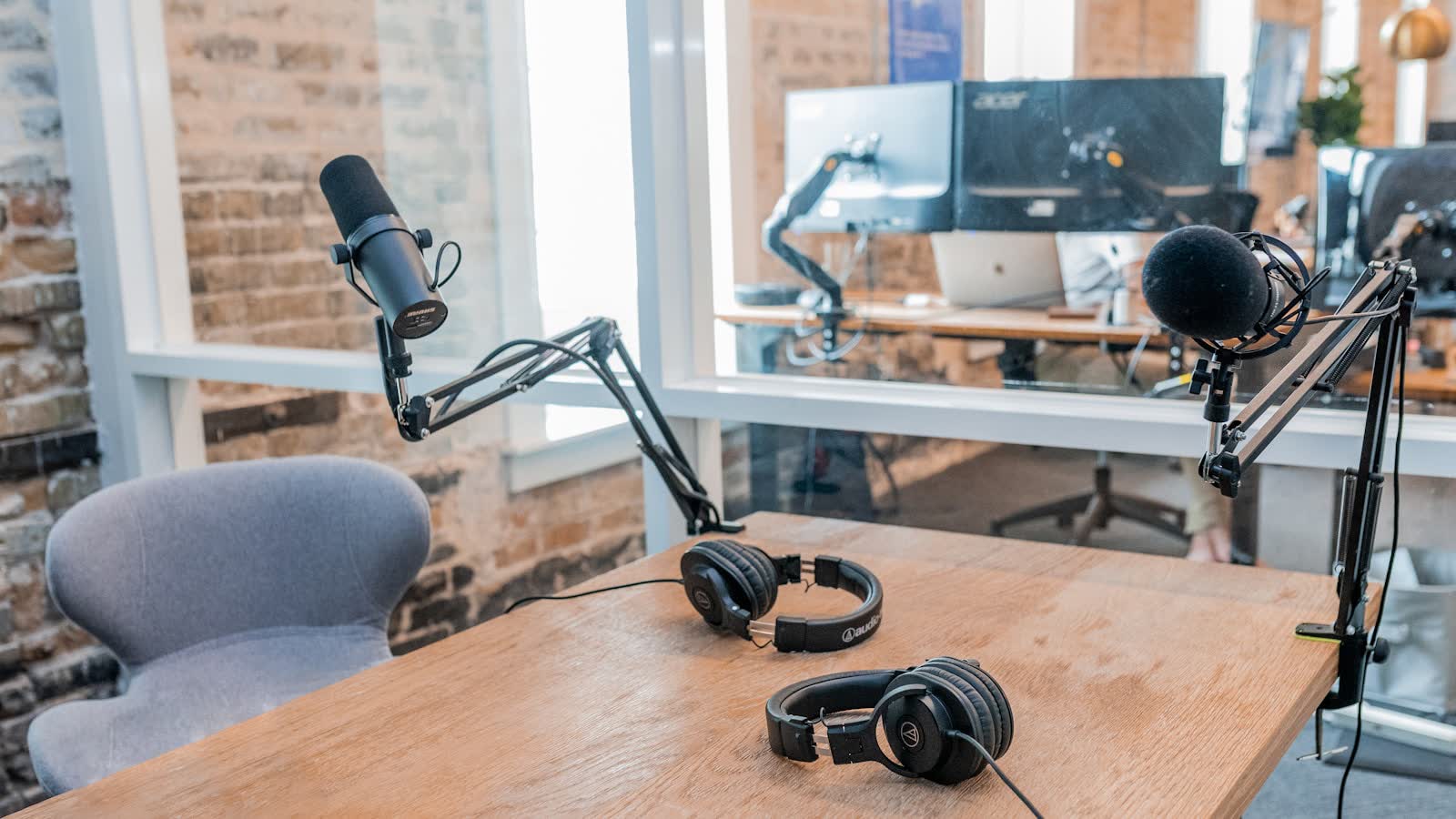 A podcasting desk with two microphones on boom arms and headphones