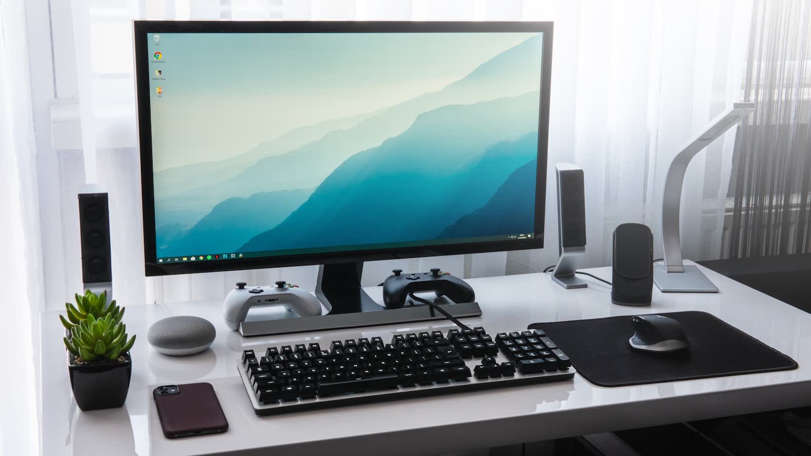 A tidy desk with a monitor, keyboard and small speakers beside a potted plant