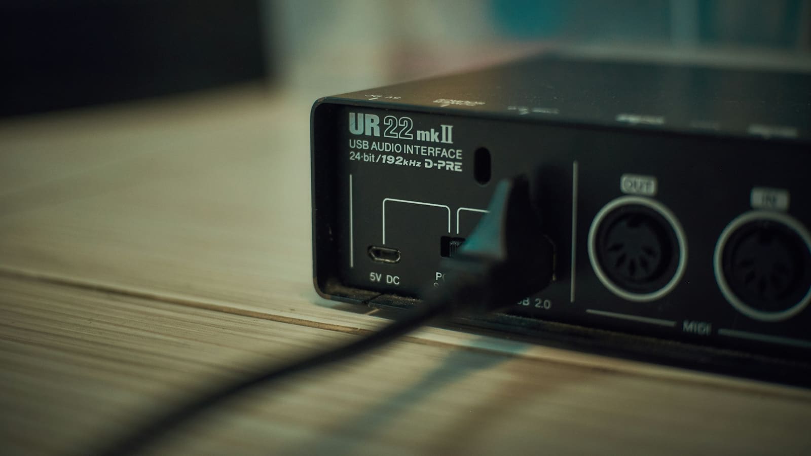 A compact USB audio interface on a wooden desk with a cable connected