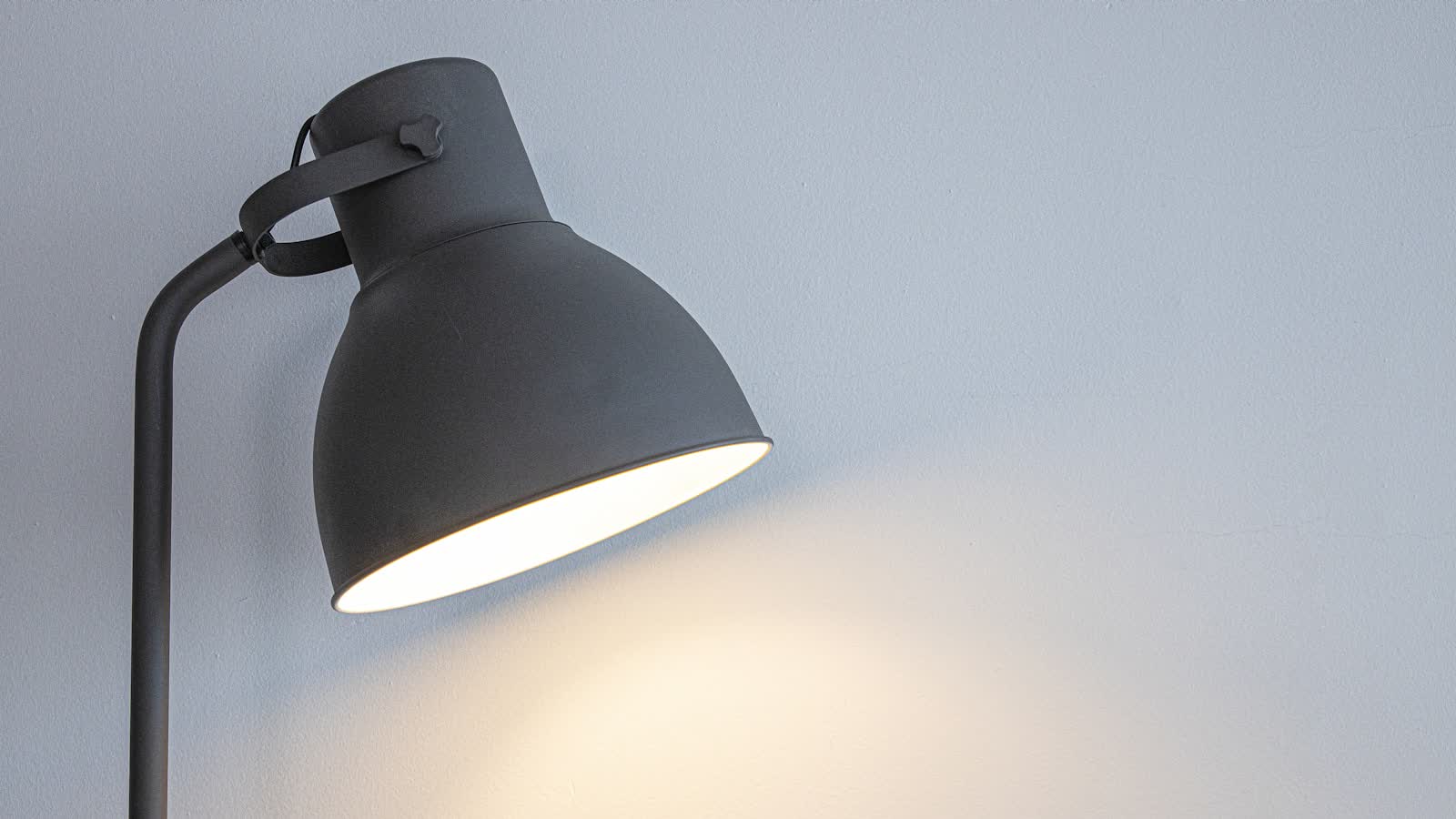 A black desk lamp switched on against a pale wall