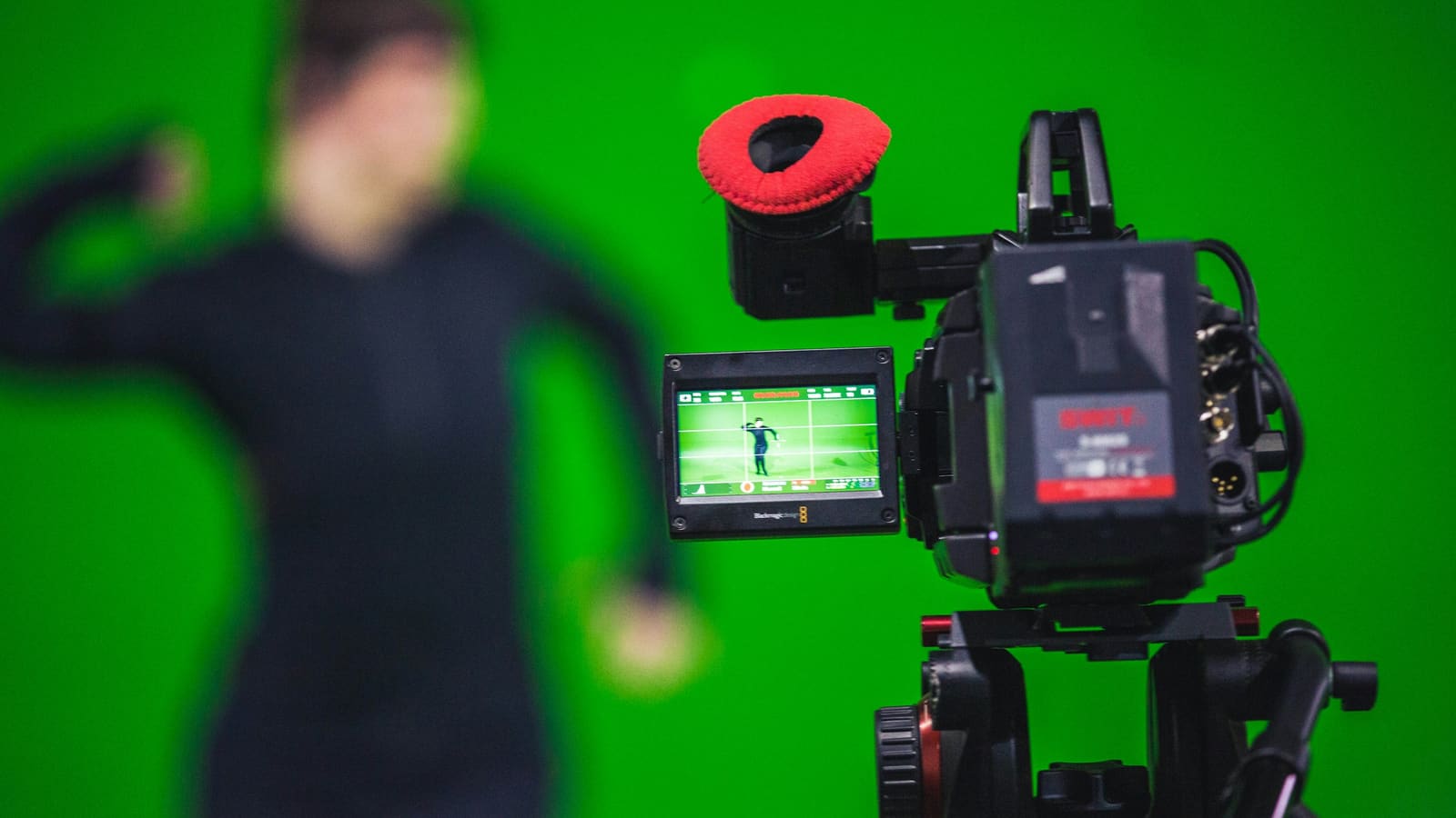 A person performing in front of a green screen with a camera on a tripod