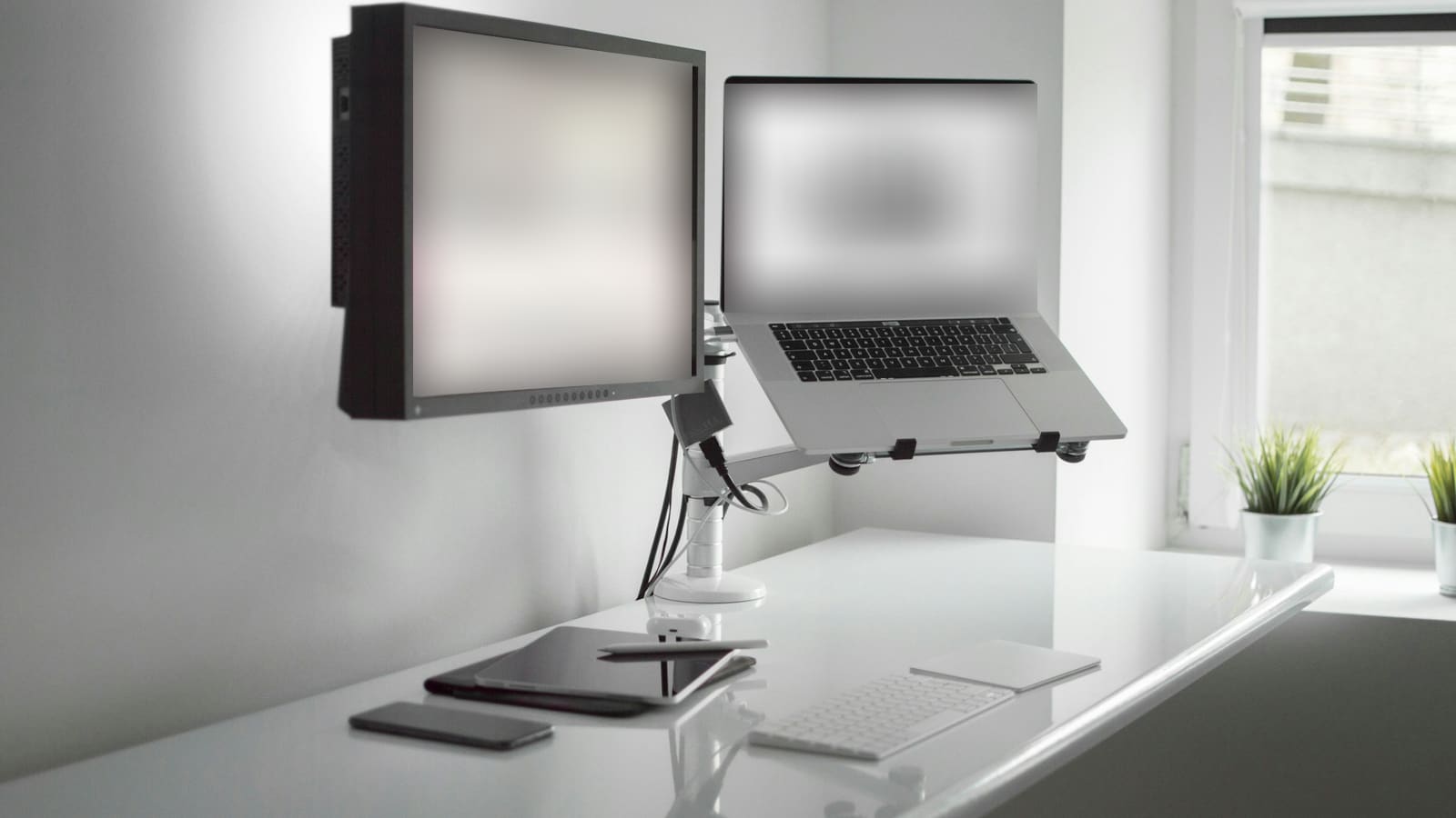 A monitor and a laptop both held on arms above a white desk