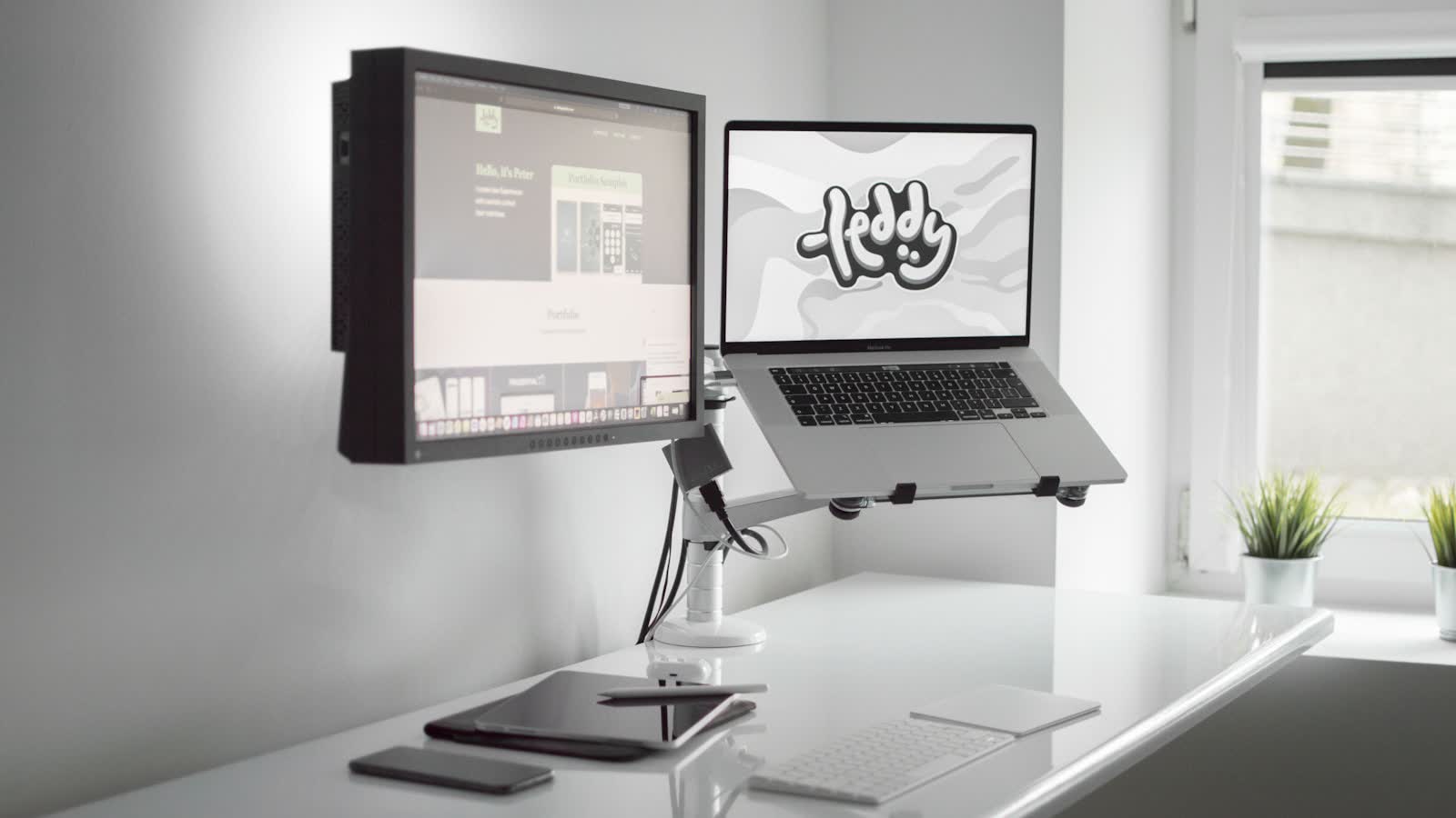 A monitor and a laptop both held on arms above a white desk