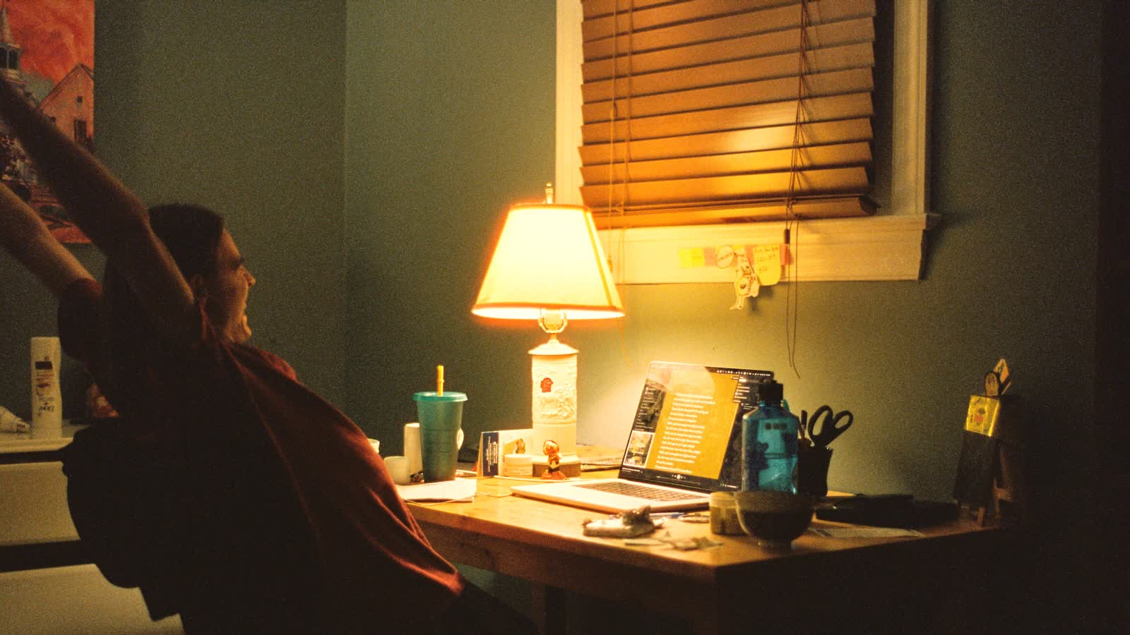 A person working at a desk lit by a warm lamp in the evening