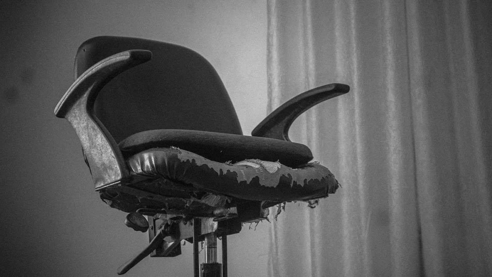 A mesh office chair by a window, photographed in black and white