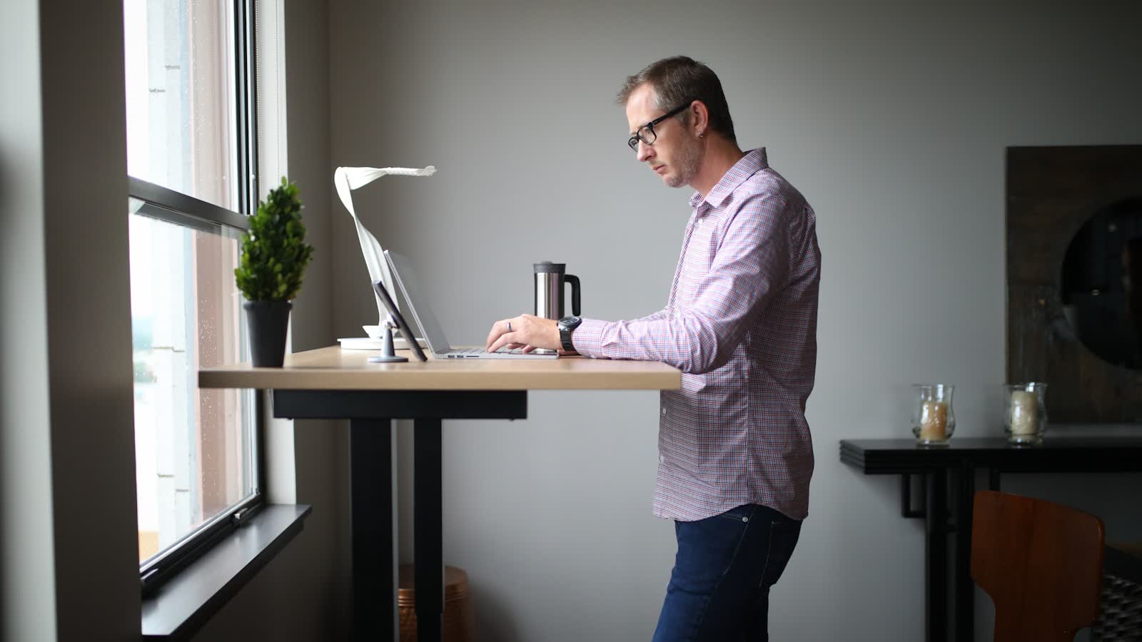 A person working at a raised standing desk beside a window