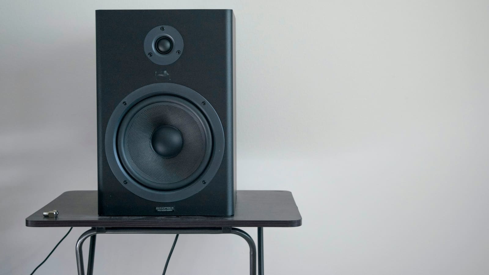 A studio monitor speaker on a stand beside a desk