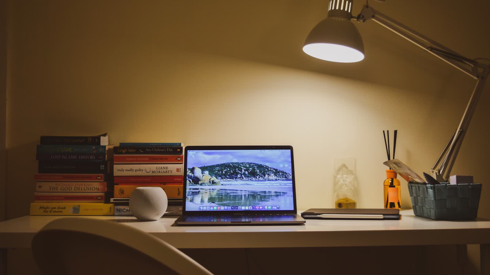 An adjustable arm lamp over a desk stacked with books and a laptop