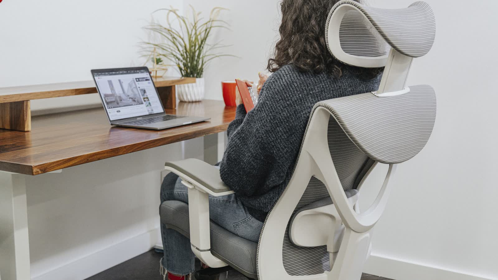 A person seated in a white mesh ergonomic chair at a desk