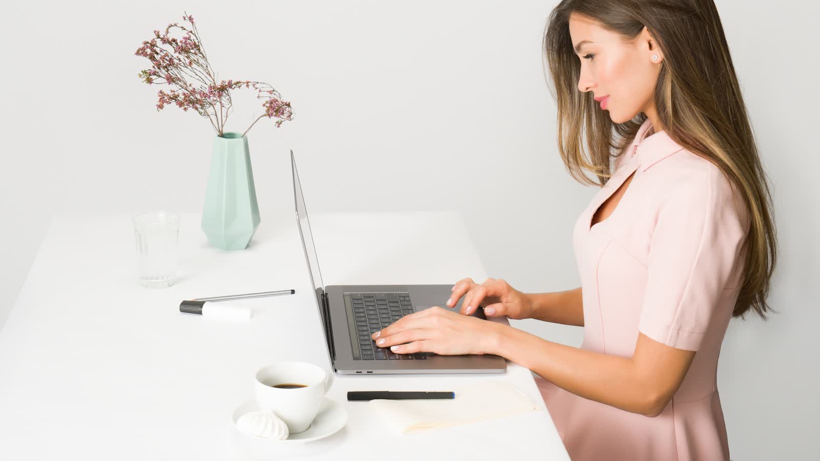 A person typing at a white desk in an upright seated posture