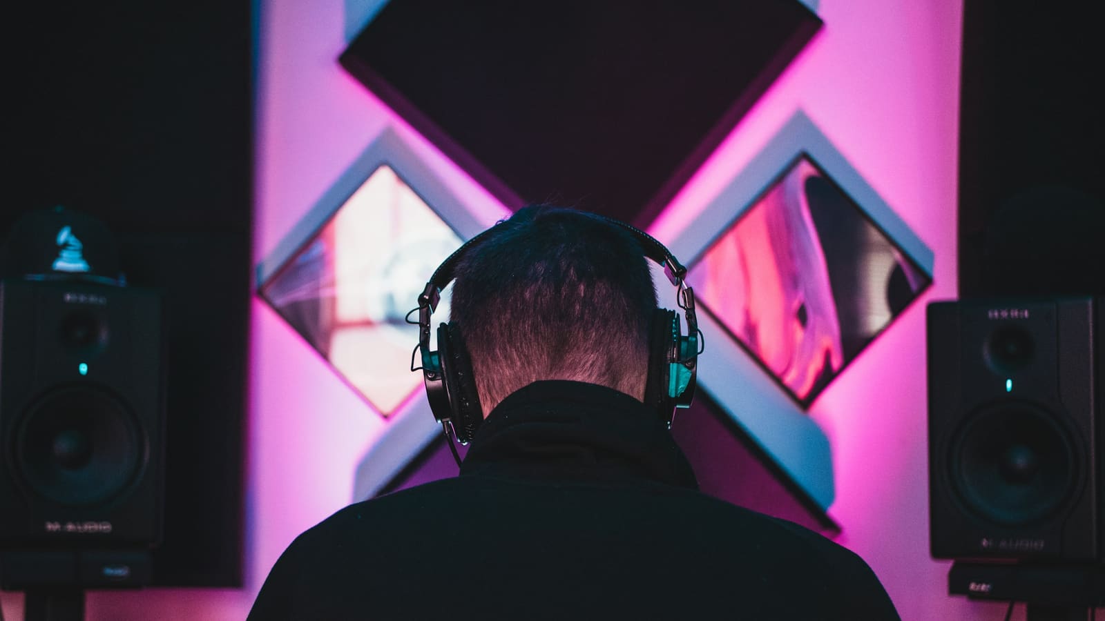 A person wearing headphones at a desk facing studio monitors