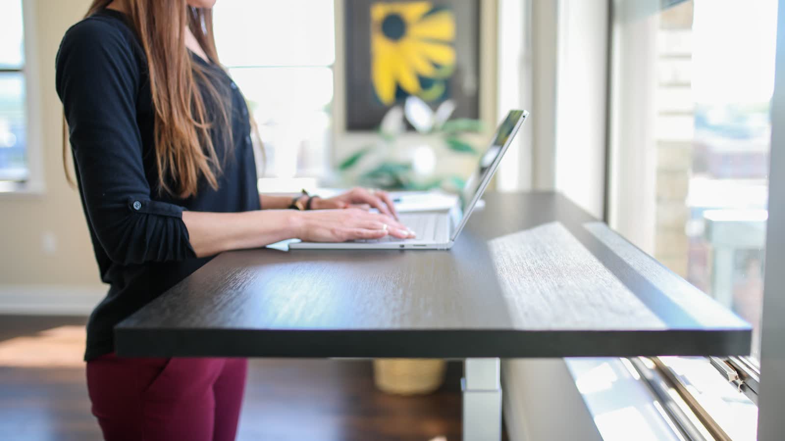 A person typing at a standing desk raised to elbow height