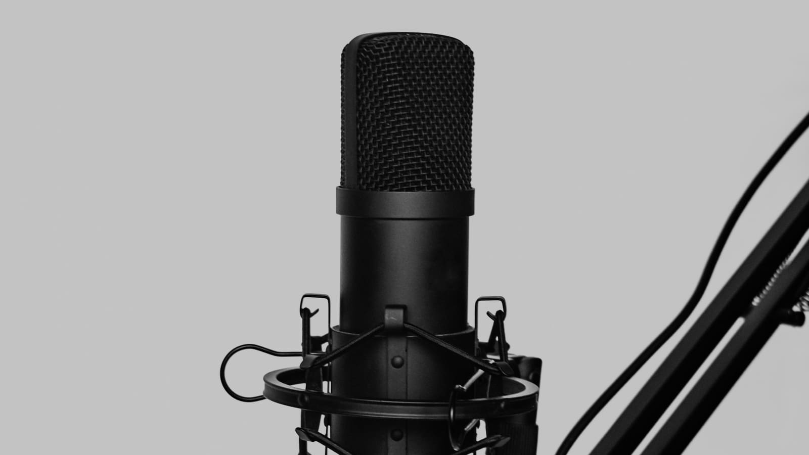 A microphone on a boom arm photographed against a plain grey wall