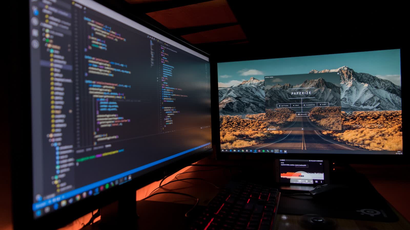 Two monitors showing code and a landscape image in a dim room