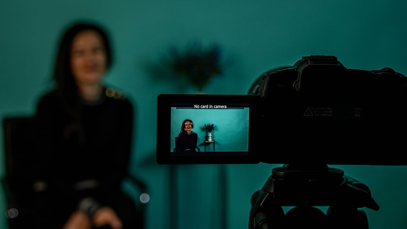 A camera on a tripod filming a person in a dim room