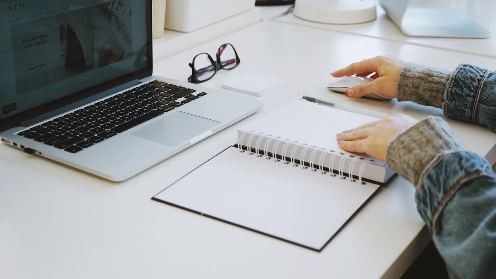 Hands typing on a laptop beside an open notebook